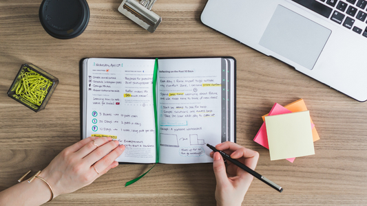 a person writing on a diary or journal with a pile of post it notes on their right