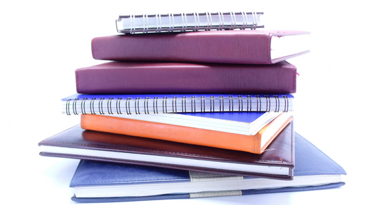 a pile of notebooks, diaries, and planners